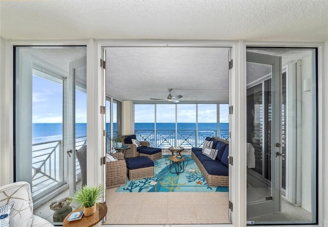 living room with expansive windows, ceiling fan, a water view, and a textured ceiling