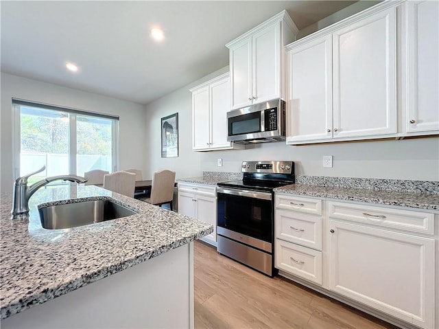 kitchen with light stone counters, appliances with stainless steel finishes, white cabinetry, a sink, and light wood-type flooring