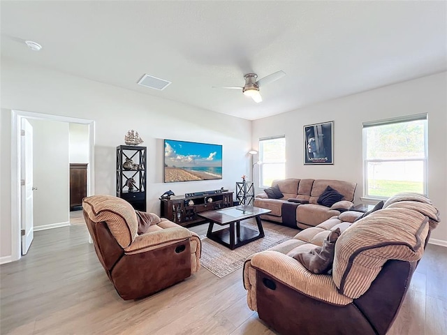 living room featuring light wood finished floors, visible vents, baseboards, and a ceiling fan