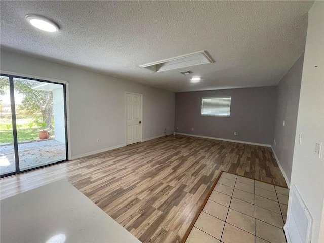 spare room with a textured ceiling, light wood-style flooring, visible vents, baseboards, and attic access