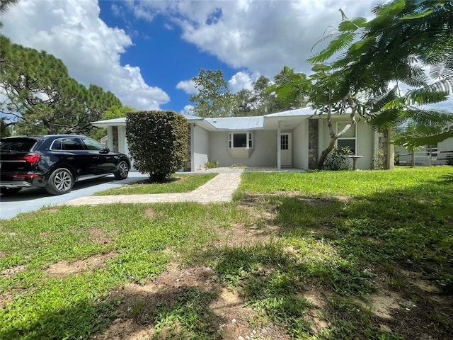 view of front of home with driveway, a front yard, metal roof, and stucco siding