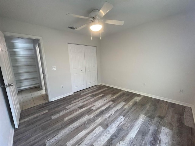 unfurnished bedroom featuring a closet, visible vents, a ceiling fan, wood finished floors, and baseboards