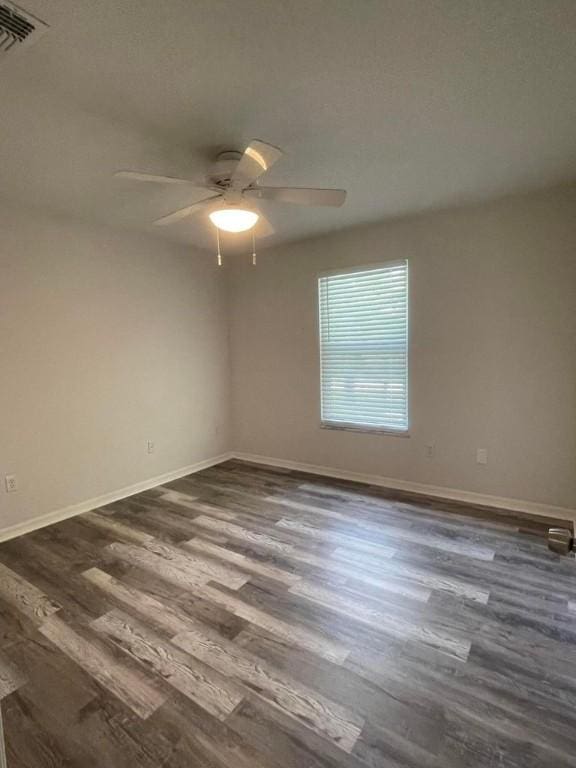 empty room featuring a ceiling fan, baseboards, and dark wood-type flooring