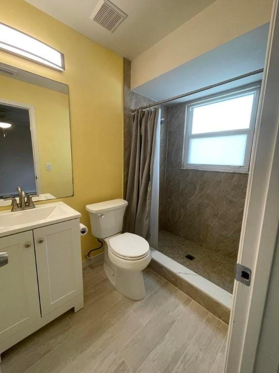 bathroom featuring visible vents, toilet, vanity, wood finished floors, and tiled shower