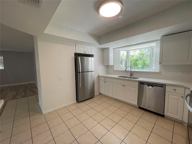 kitchen featuring light tile patterned floors, appliances with stainless steel finishes, white cabinets, and a sink