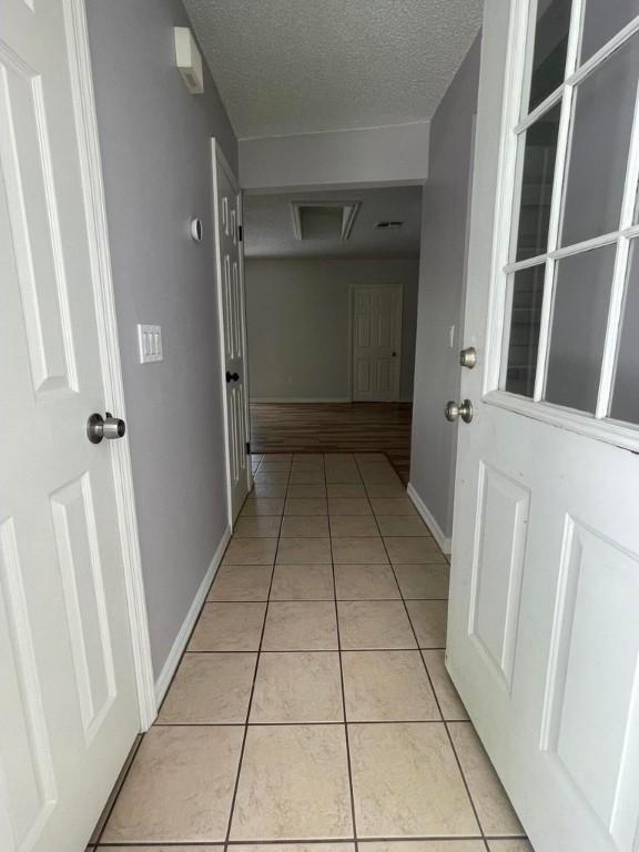 hall featuring a textured ceiling, baseboards, and light tile patterned floors