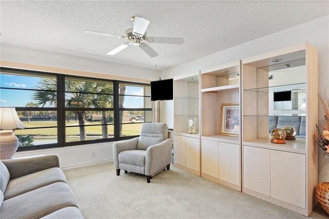 living area with a ceiling fan, a textured ceiling, and light colored carpet