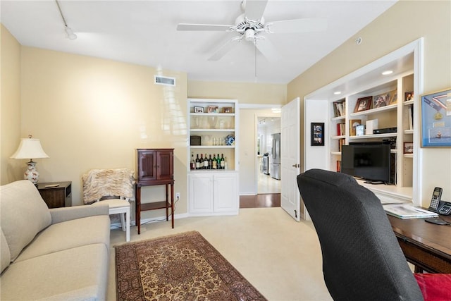 office featuring built in shelves, visible vents, a ceiling fan, light carpet, and track lighting