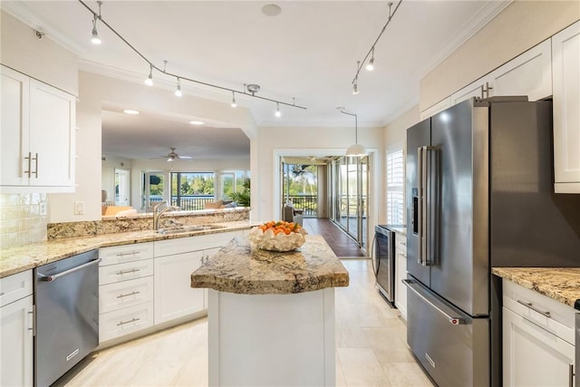 kitchen featuring light stone counters, a center island, stainless steel appliances, white cabinetry, and a sink