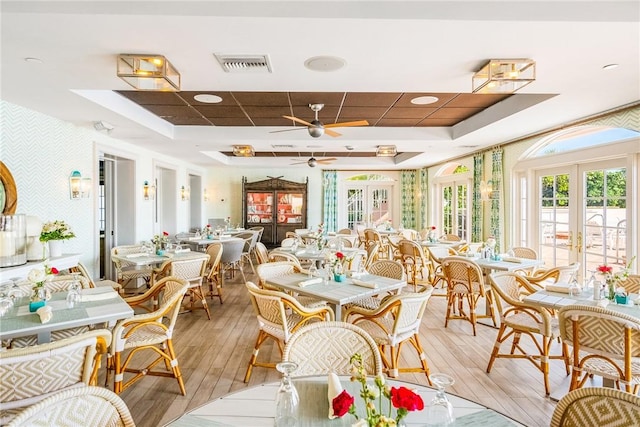 dining room featuring ceiling fan, visible vents, light wood-style floors, french doors, and a raised ceiling