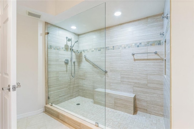 bathroom with a tile shower, tile patterned flooring, visible vents, and baseboards