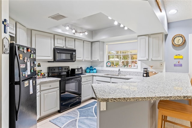 kitchen featuring sink, a breakfast bar, black appliances, kitchen peninsula, and a raised ceiling