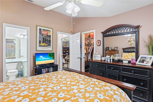 bedroom with a spacious closet, ensuite bath, a textured ceiling, vaulted ceiling, and ceiling fan