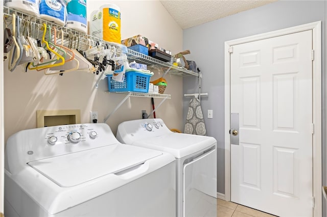 clothes washing area with separate washer and dryer, a textured ceiling, and light tile patterned floors