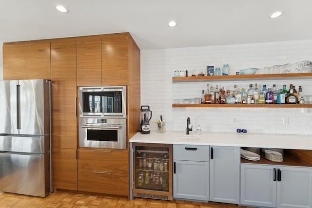 bar featuring sink, gray cabinetry, beverage cooler, stainless steel appliances, and light parquet flooring