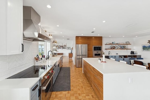 kitchen with white cabinets, island exhaust hood, stainless steel appliances, light parquet flooring, and a spacious island