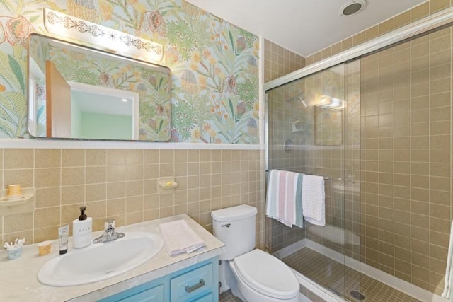 bathroom featuring vanity, a shower with door, tile walls, and toilet