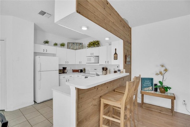 kitchen featuring a kitchen bar, visible vents, a peninsula, white appliances, and white cabinetry