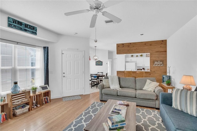 living room with wooden walls, a ceiling fan, baseboards, wood finished floors, and visible vents