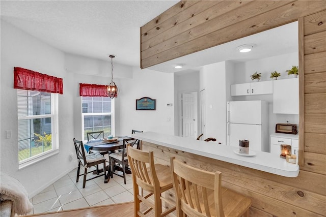 kitchen with white cabinets, a kitchen breakfast bar, freestanding refrigerator, a peninsula, and pendant lighting