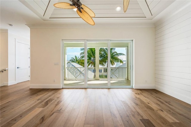 empty room featuring ceiling fan, baseboards, hardwood / wood-style floors, and wood walls