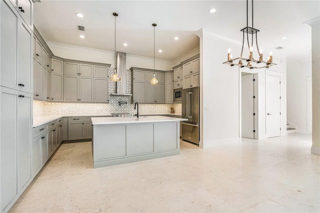 kitchen featuring backsplash, gray cabinetry, wall chimney range hood, a center island with sink, and stainless steel appliances