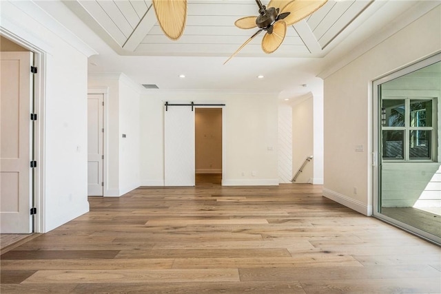 empty room with a ceiling fan, baseboards, ornamental molding, a barn door, and light wood-type flooring