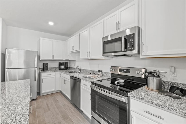 kitchen featuring light stone countertops, white cabinetry, sink, light hardwood / wood-style floors, and appliances with stainless steel finishes