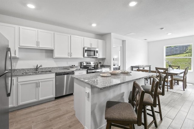 kitchen featuring a center island, white cabinets, sink, appliances with stainless steel finishes, and light stone counters