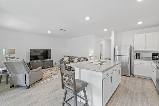 kitchen with stainless steel refrigerator, white cabinetry, a center island, a breakfast bar area, and light wood-type flooring