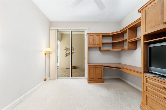 unfurnished office featuring light carpet, built in desk, and ceiling fan