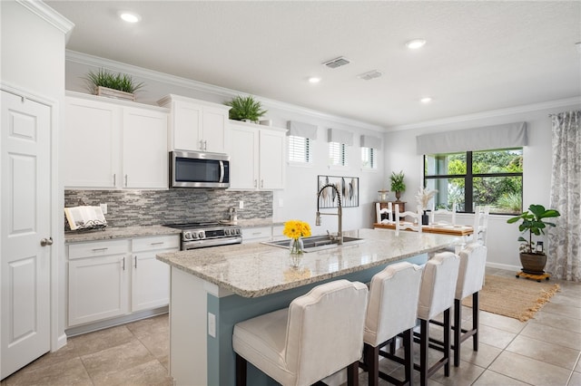 kitchen featuring stainless steel appliances, a center island with sink, sink, ornamental molding, and white cabinetry