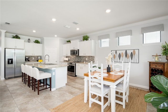 kitchen with stainless steel appliances, white cabinetry, sink, ornamental molding, and a kitchen island with sink