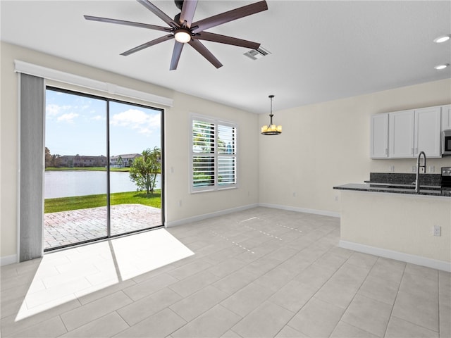 interior space with dark stone counters, decorative light fixtures, a water view, white cabinets, and light tile patterned flooring