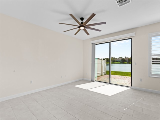 empty room with ceiling fan, a water view, and light tile patterned floors