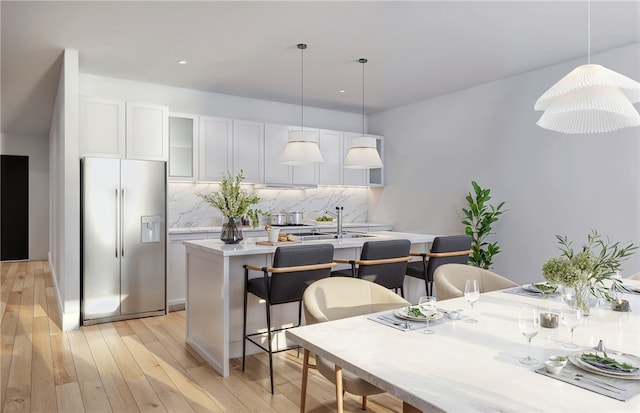 kitchen with a center island with sink, a breakfast bar, stainless steel refrigerator with ice dispenser, hanging light fixtures, and light hardwood / wood-style flooring