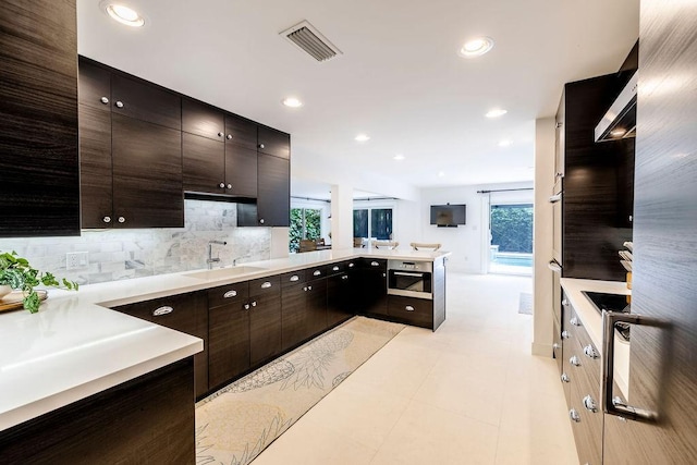 kitchen with dark brown cabinetry, sink, backsplash, and stainless steel oven