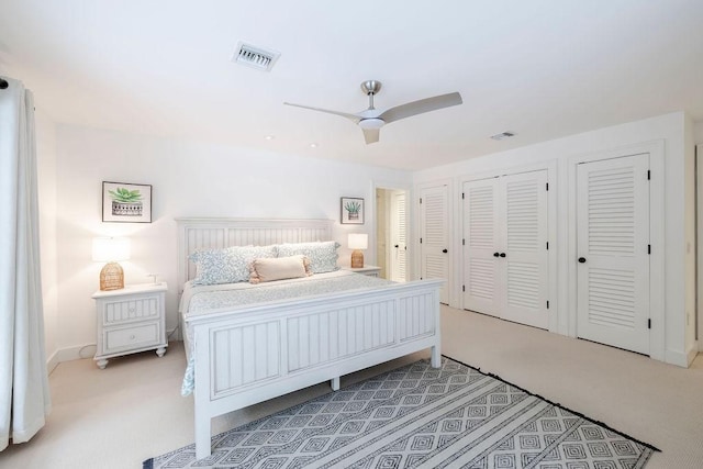 bedroom with ceiling fan, light carpet, and two closets