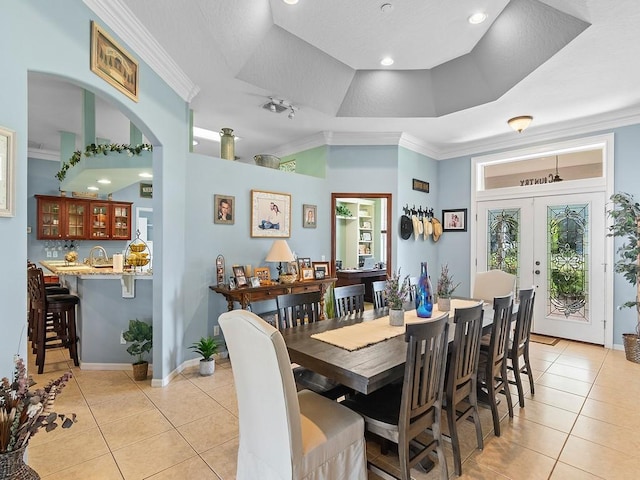 tiled dining space featuring sink, crown molding, a raised ceiling, and french doors