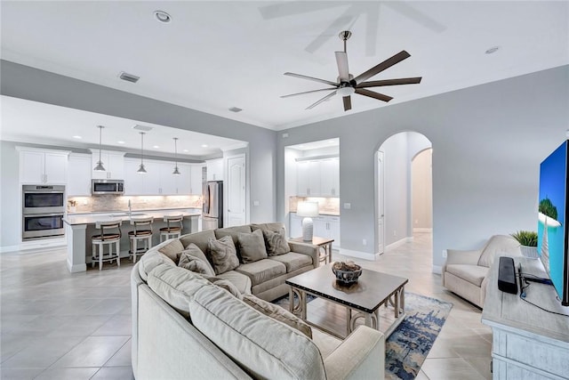 tiled living room featuring ceiling fan, crown molding, and sink