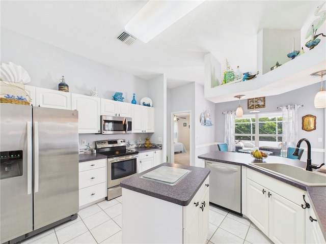 kitchen with a kitchen island, a sink, appliances with stainless steel finishes, white cabinetry, and dark countertops