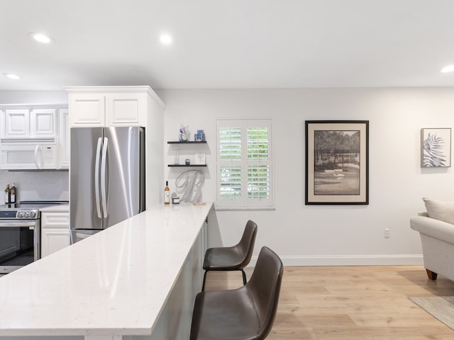 kitchen with white cabinets, a kitchen bar, light wood-type flooring, and appliances with stainless steel finishes