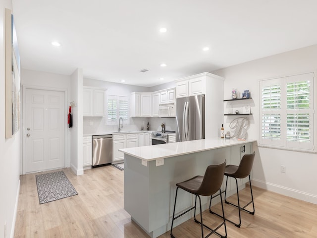 kitchen featuring white cabinetry, kitchen peninsula, stainless steel appliances, and a healthy amount of sunlight