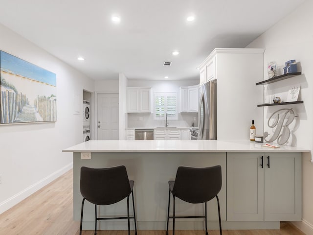 kitchen featuring light hardwood / wood-style floors, stainless steel appliances, stacked washing maching and dryer, sink, and white cabinetry