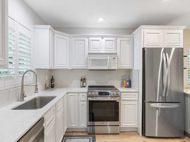 kitchen with stainless steel appliances, light wood-type flooring, decorative backsplash, sink, and white cabinets