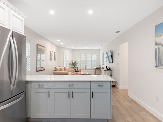 kitchen with light wood-type flooring, kitchen peninsula, stainless steel refrigerator, and white cabinets