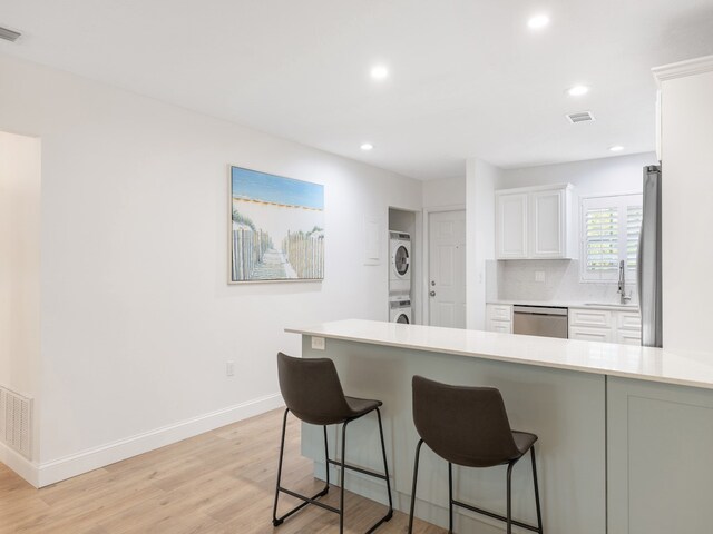 kitchen with sink, appliances with stainless steel finishes, stacked washing maching and dryer, white cabinets, and light wood-type flooring