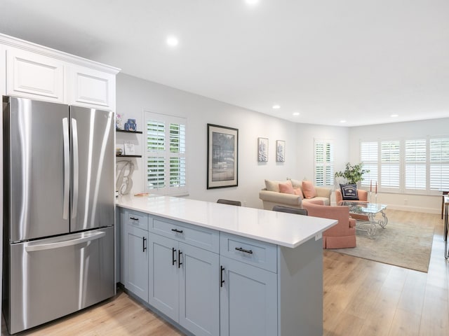 kitchen with white cabinetry, kitchen peninsula, light wood-type flooring, and stainless steel fridge