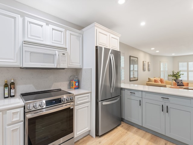 kitchen with white cabinets, gray cabinets, backsplash, light wood-type flooring, and appliances with stainless steel finishes