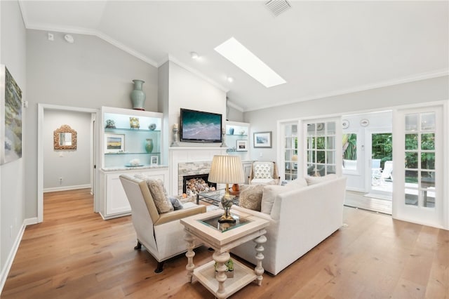 living room with vaulted ceiling with skylight, ornamental molding, and light hardwood / wood-style flooring